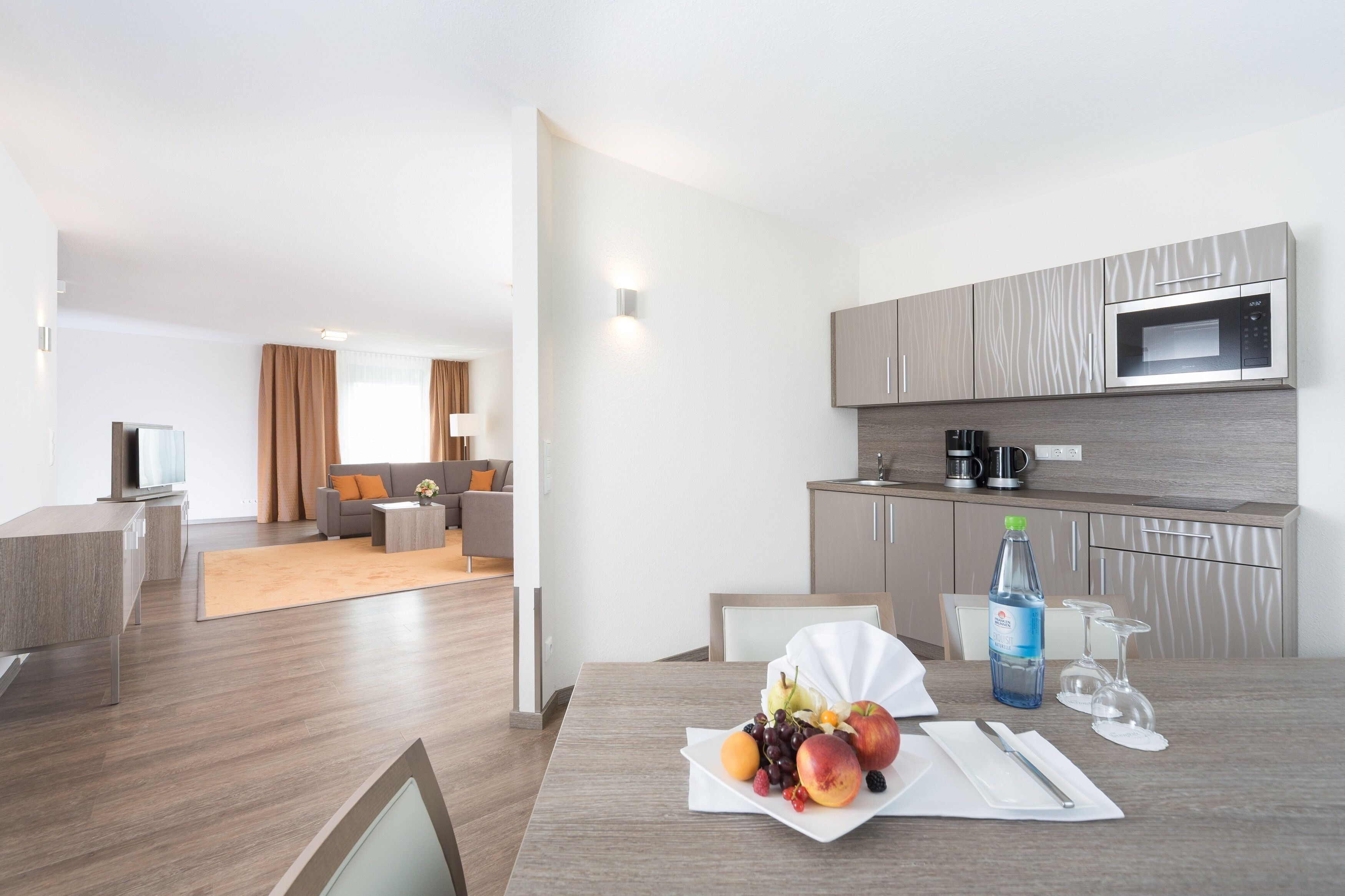 A modern hotel room with a dining area, kitchenette, and a living space.