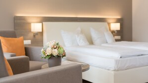 A hotel room with a bed, a chair, a small table, and a vase of flowers. - HerzogsPark Studios & Apartments (Herzogenaurach)