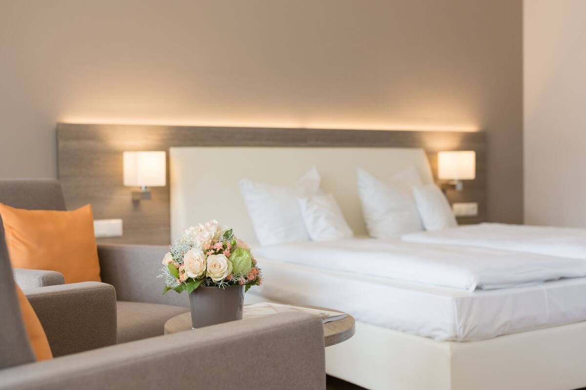 Ein Hotelzimmer mit einem Bett, einem Sessel, einem kleinen Tisch und einer Blumenvase.