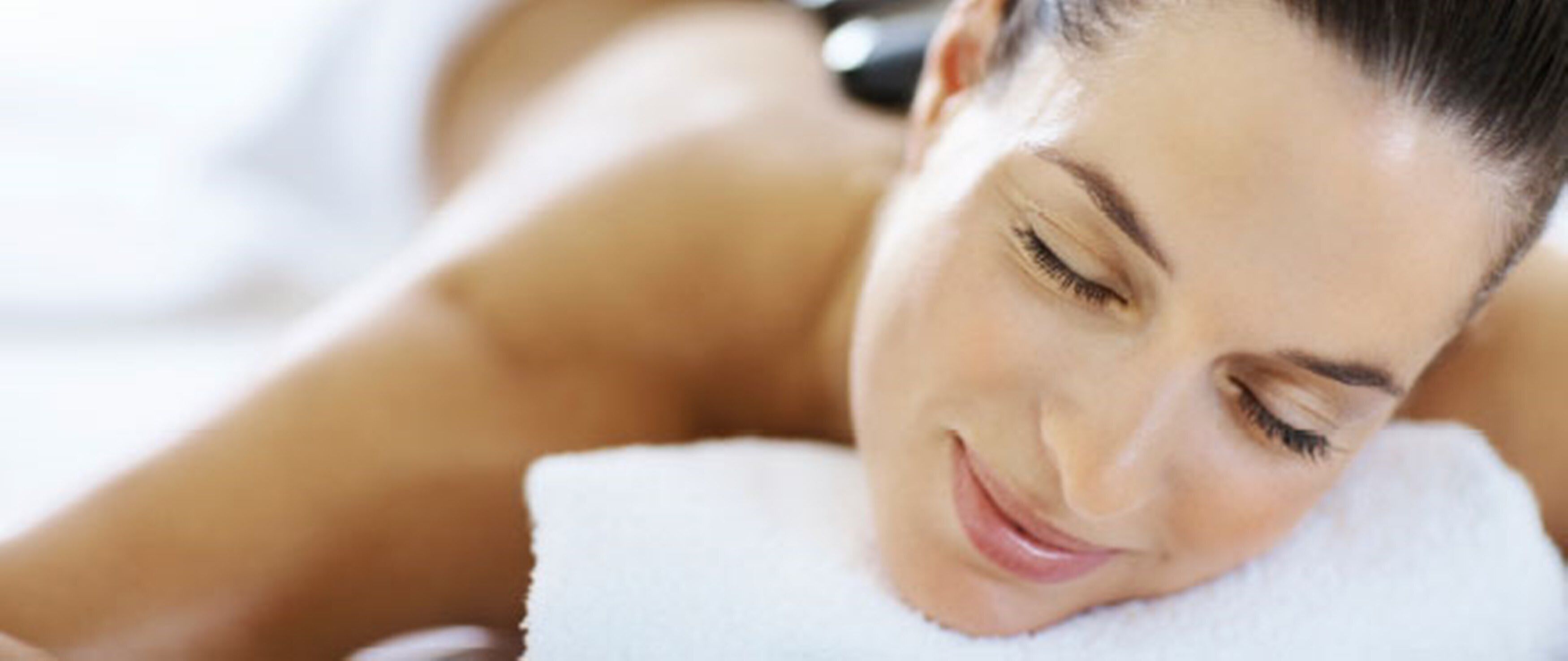 A person lying down with a white towel, suggesting a spa or relaxation setting.