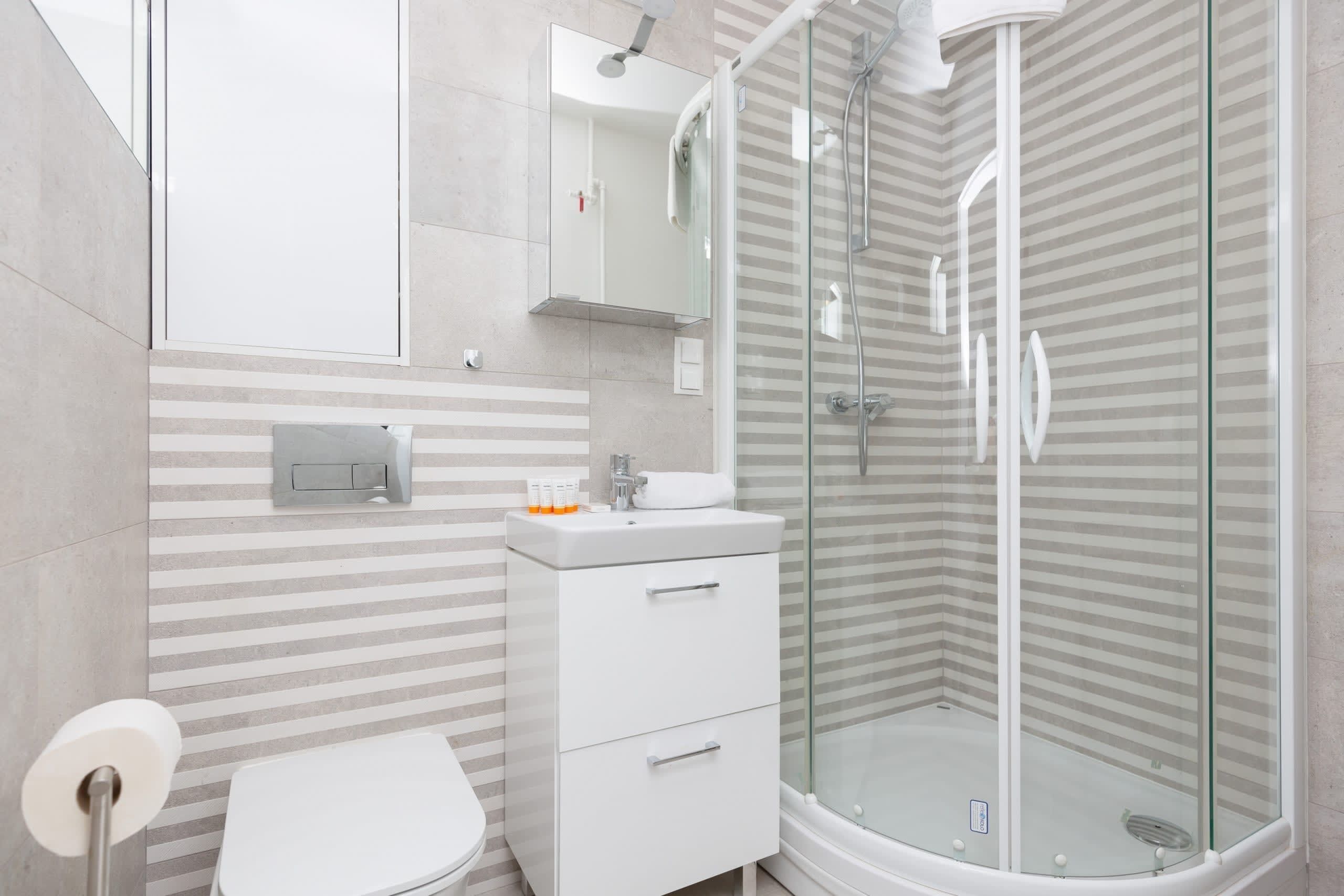 Un baño moderno con cabina de ducha de vidrio, un lavabo blanco y un diseño de pared a rayas.