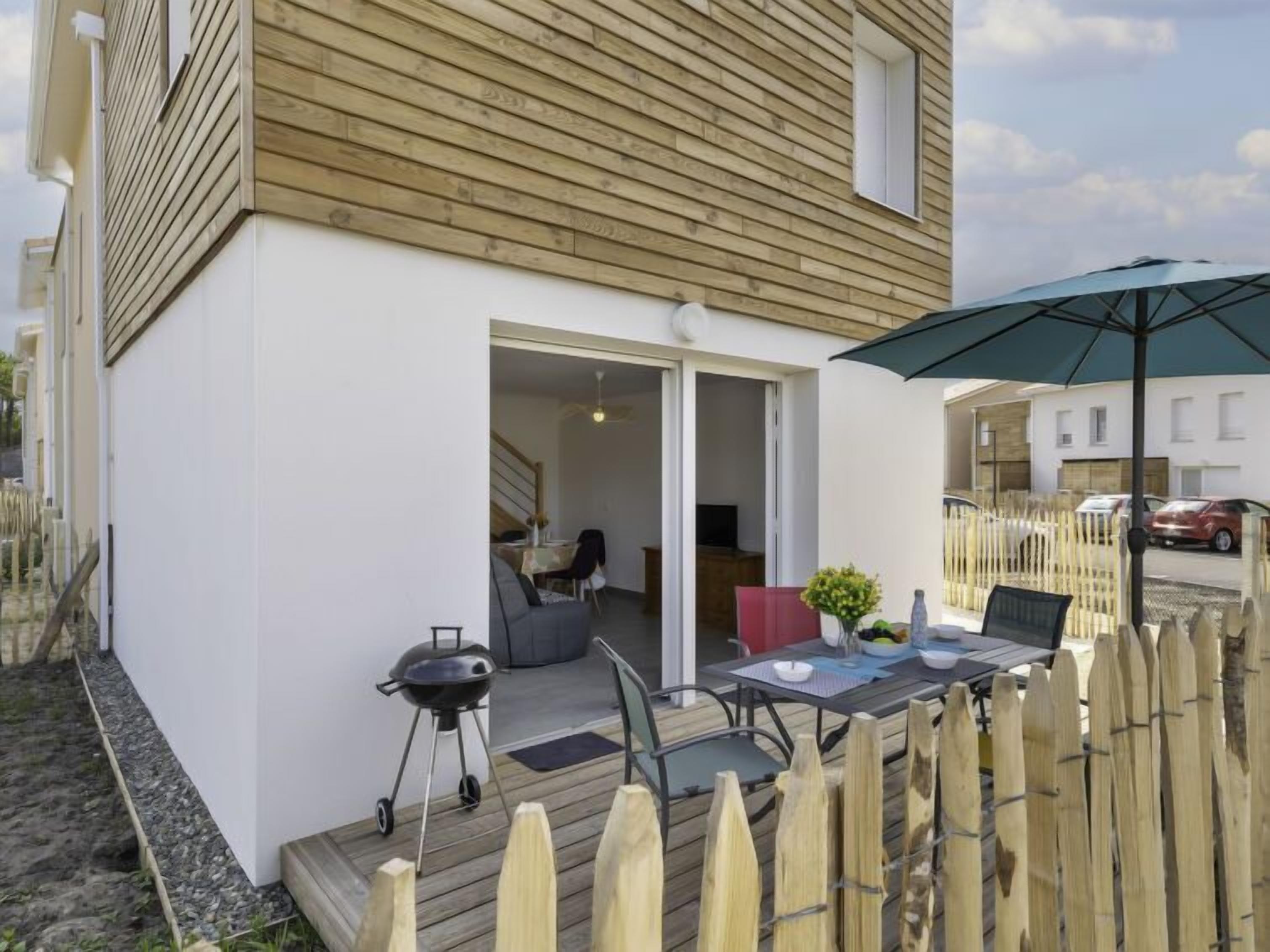 Una casa moderna amb una terrassa de fusta, una barbacoa i una zona de dinar amb mobles d'exterior.