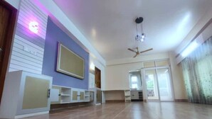Ein geräumiges Zimmer mit Holzboden, Deckenventilator und großem Fenster.