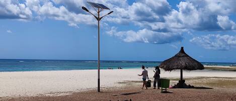 A beach with a thatched umbrella and a solar-powered street lamp.