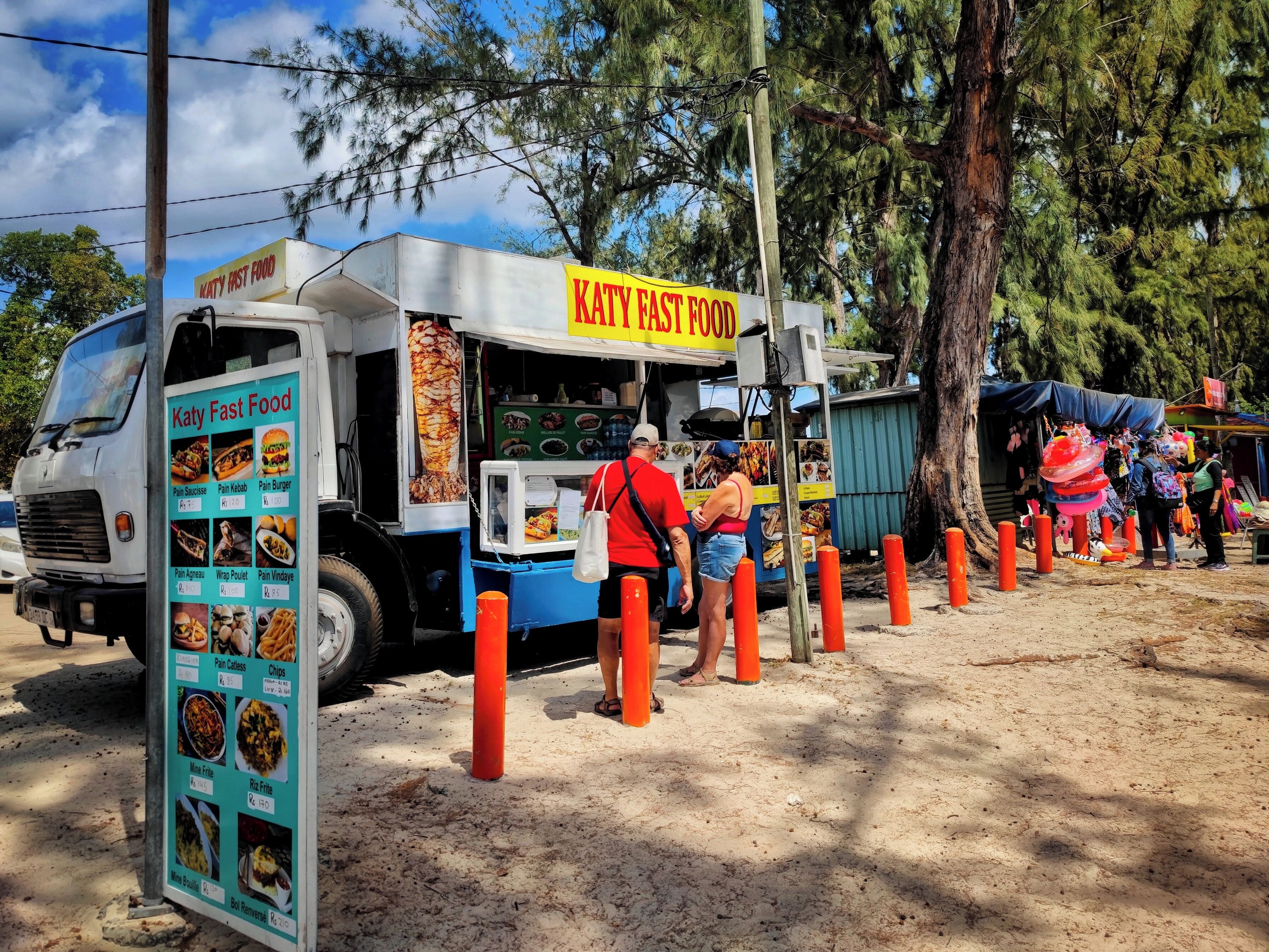 Un camión de comida llamado "Katy Fast Food" con un cartel de menú que muestra diferentes opciones.