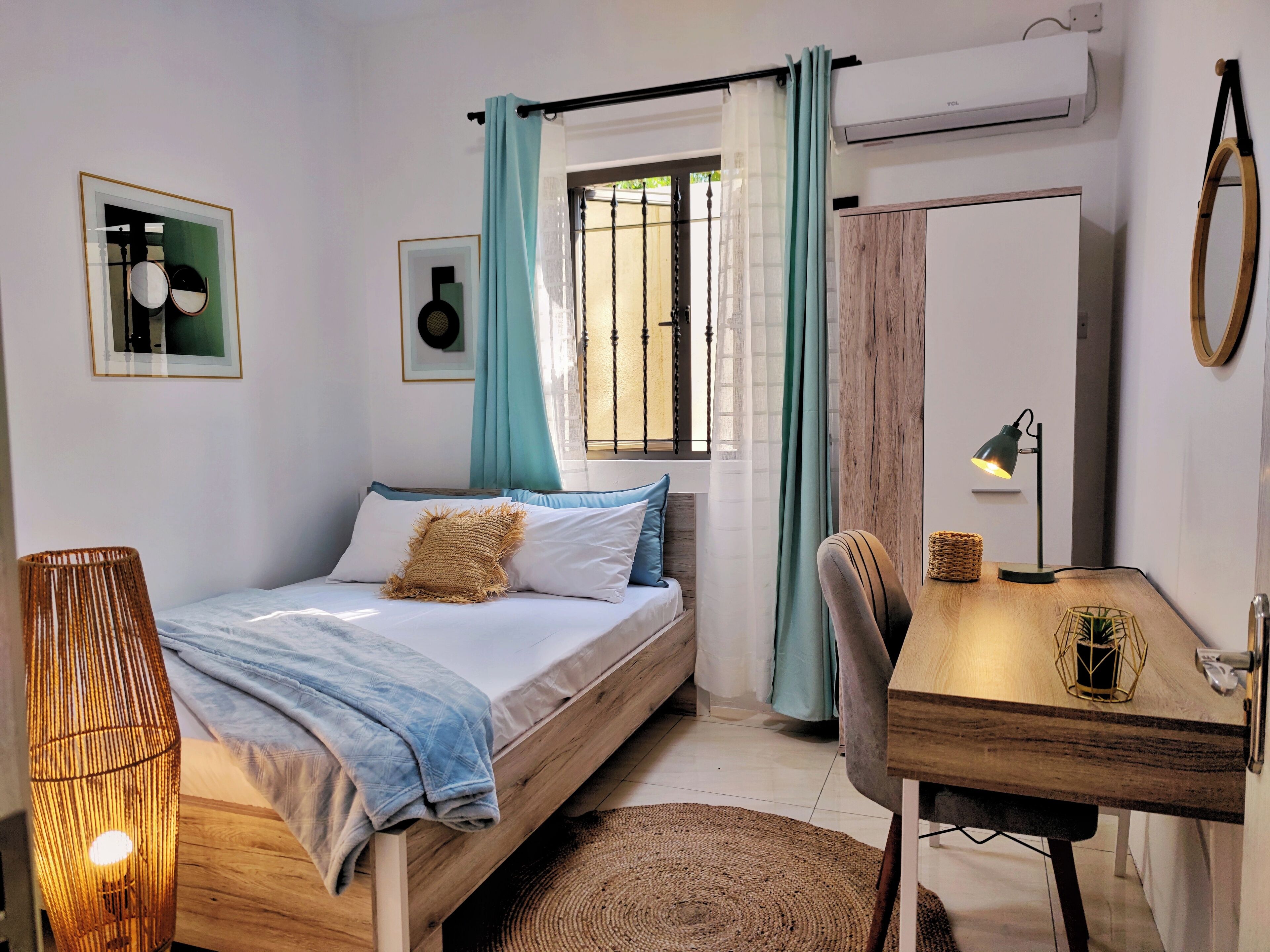 A bedroom with a bed, a desk, a chair, a lamp, a hanging basket, and a window with curtains.
