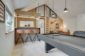 A modern bar area with a pool table, three bar stools, and a sofa.