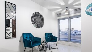 Una sala de estar moderna con dos sillones azul verdosos, una obra de arte redonda en la pared y un ventanal con vistas a la ciudad.
