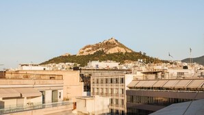 Un paisaje urbano con una colina destacada al fondo, edificios modernos de techos planos y un cielo despejado.