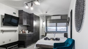 Un dormitorio moderno con una cama, una silla azul, un televisor y una ventana con vistas a la ciudad.