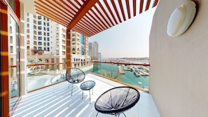 A balcony with two chairs, a view of a marina, and high-rise buildings in the background. - Tanin - Glowing Studio With Sea View Near Burj Al Arab (Dubai)