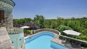 En swimmingpool med en stenvæg, omgivet af frodig vegetation og en klar, blå himmel.