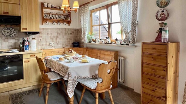 A cozy kitchen with wooden cabinets, a dining table set for four, and a window with curtains.