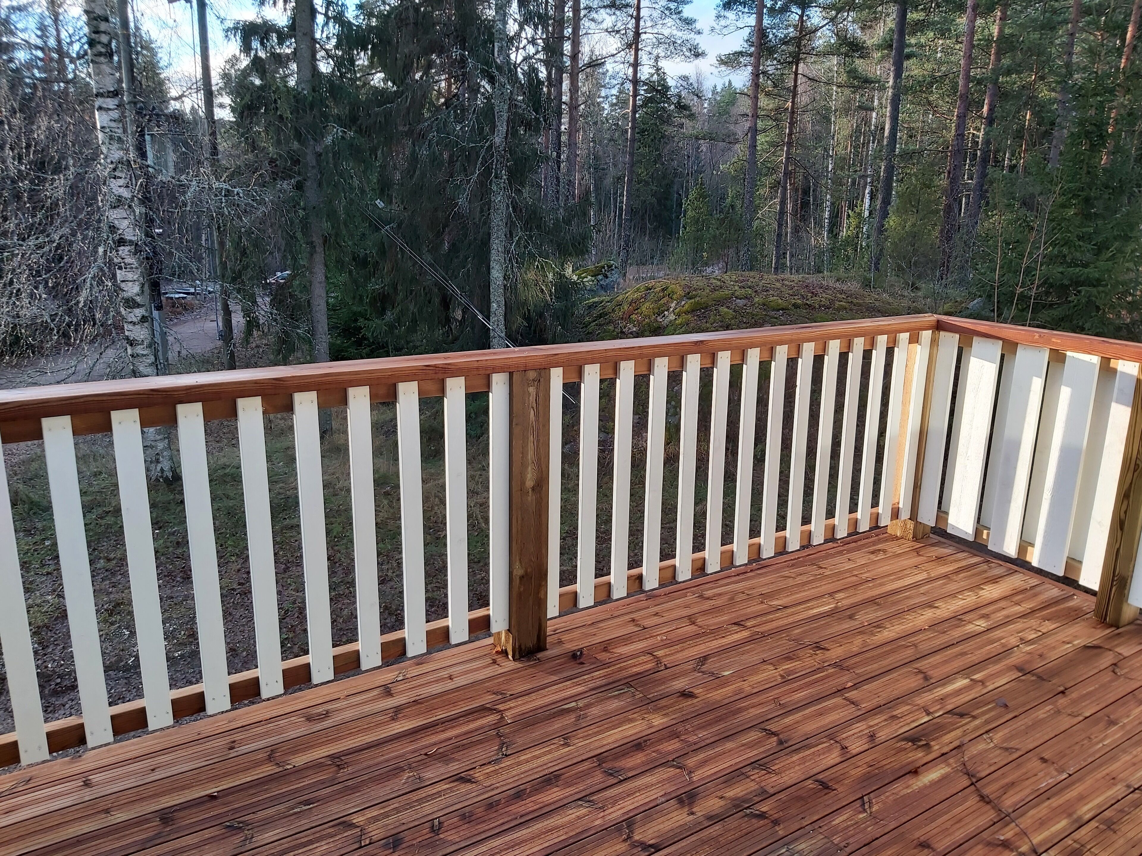 A wooden deck with white railings, surrounded by a forested area.