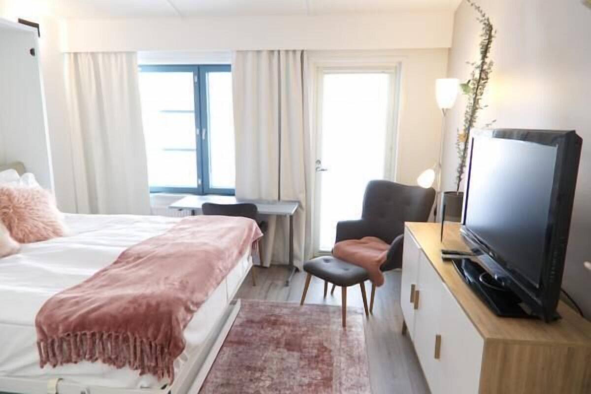 Ett hotellrum med en säng, ett skrivbord, en tv och en stol.