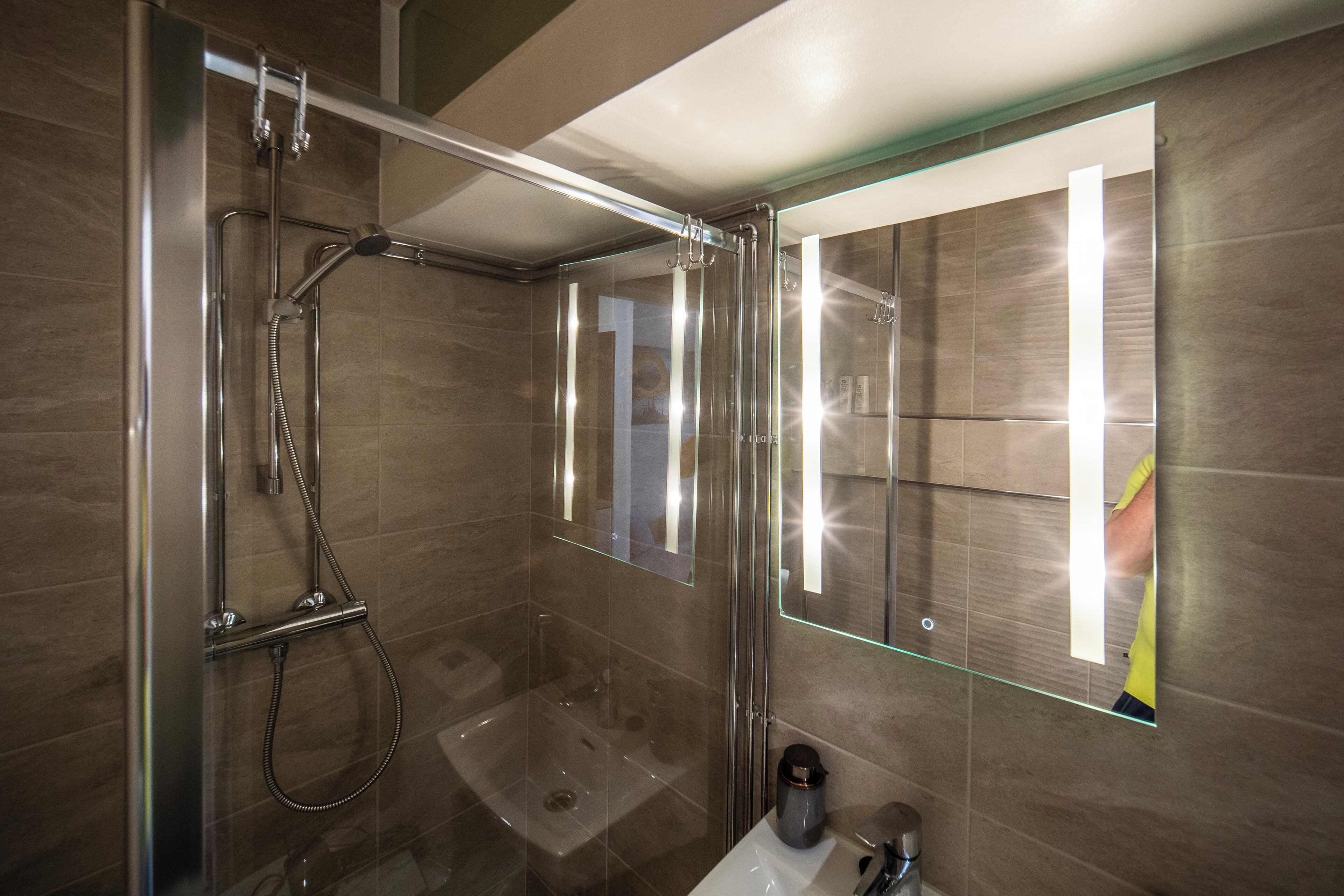Ein modernes Badezimmer mit einer gläsernen Duschkabine, einem Waschbecken und einem Spiegel.