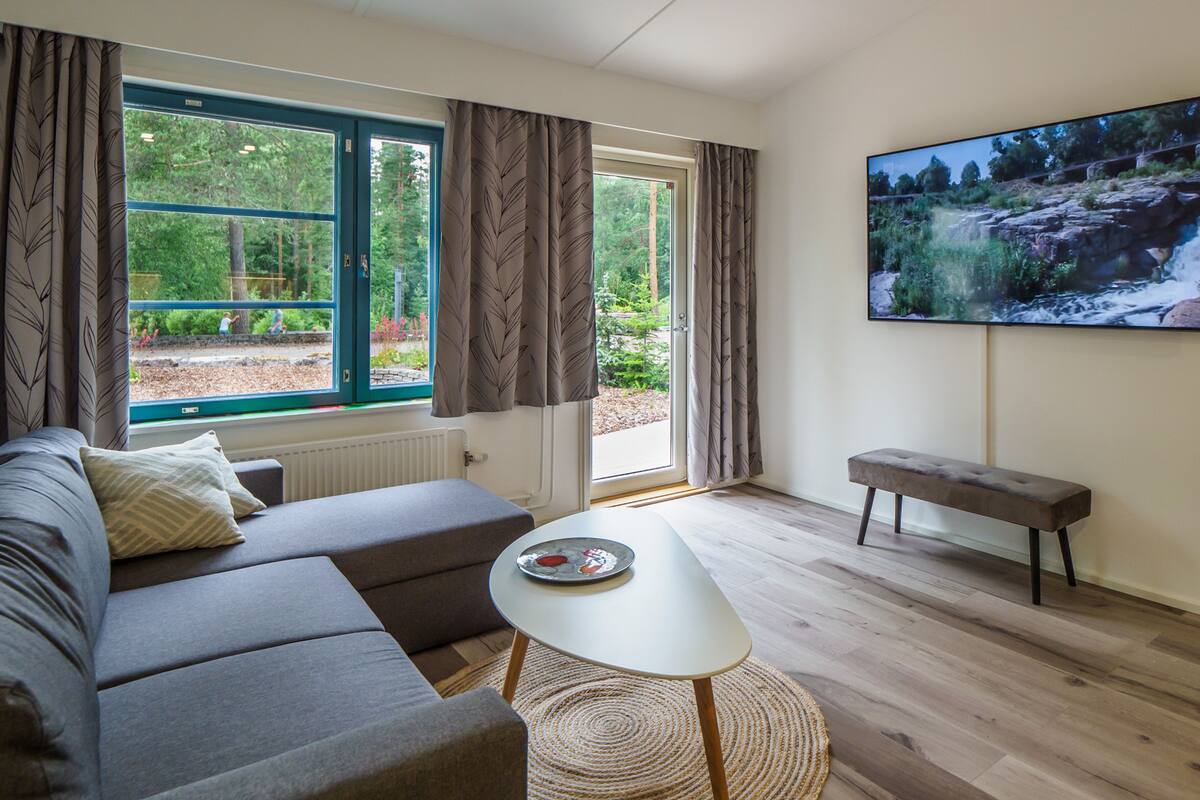 Ett modernt vardagsrum med en soffa, ett litet bord, en bänk och en stor TV-skärm som visar ett naturbild.