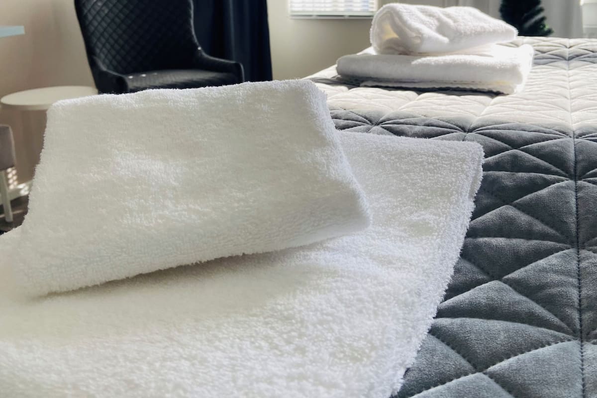 Ett hotellrum med två sängar, var och en med en vit handduk och ett grått, vadderat sängöverkast. Det finns en stol och ett litet bord i rummet.