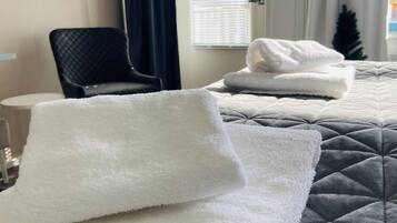 Quarto de hotel com duas camas, cada uma com uma toalha branca e um edredom cinza acolchoado. Há uma cadeira e uma pequena mesa no quarto.