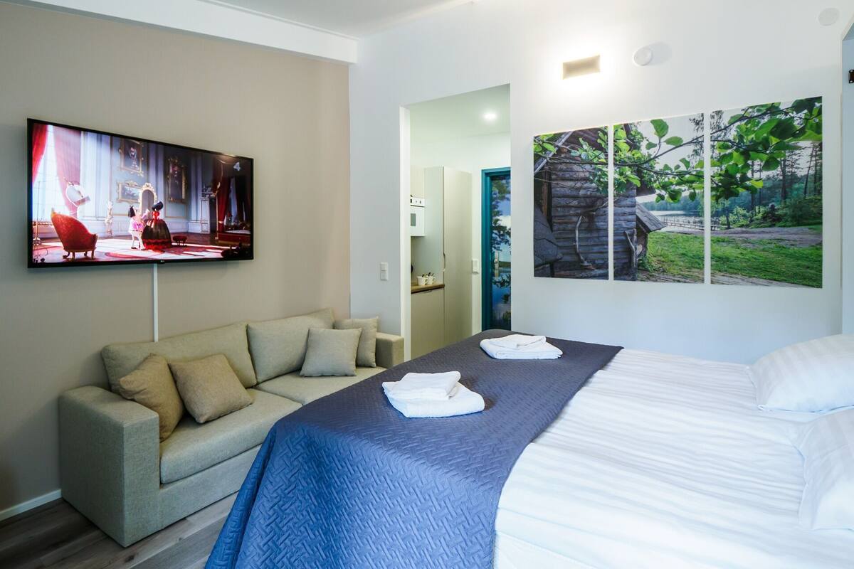 Ett hotellrum med en säng, en soffa, en tv och en vägg prydd med ett naturmotiv.