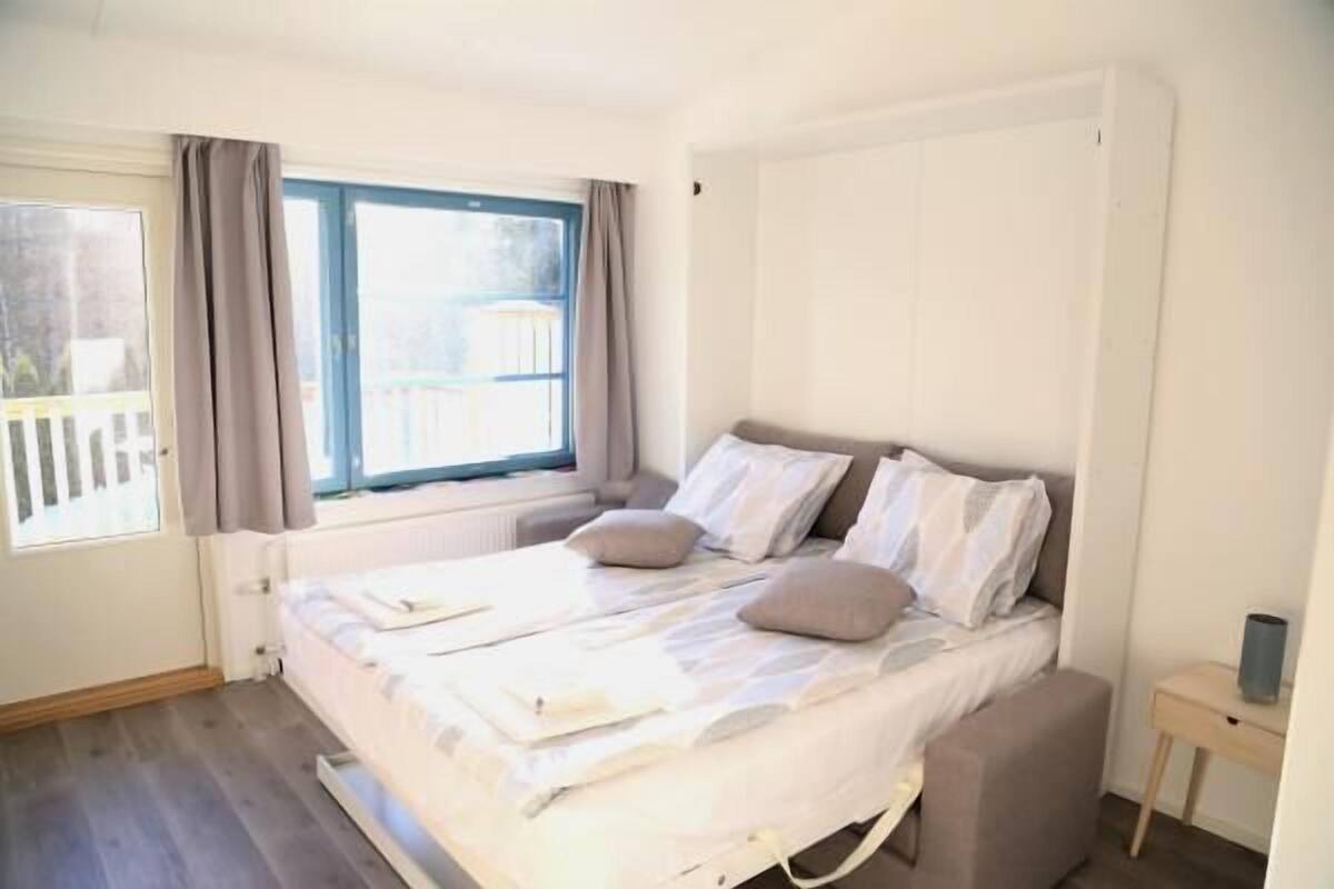 Ett sovrum med en säng, ett fönster med gardiner, ett nattduksbord och ett element.
