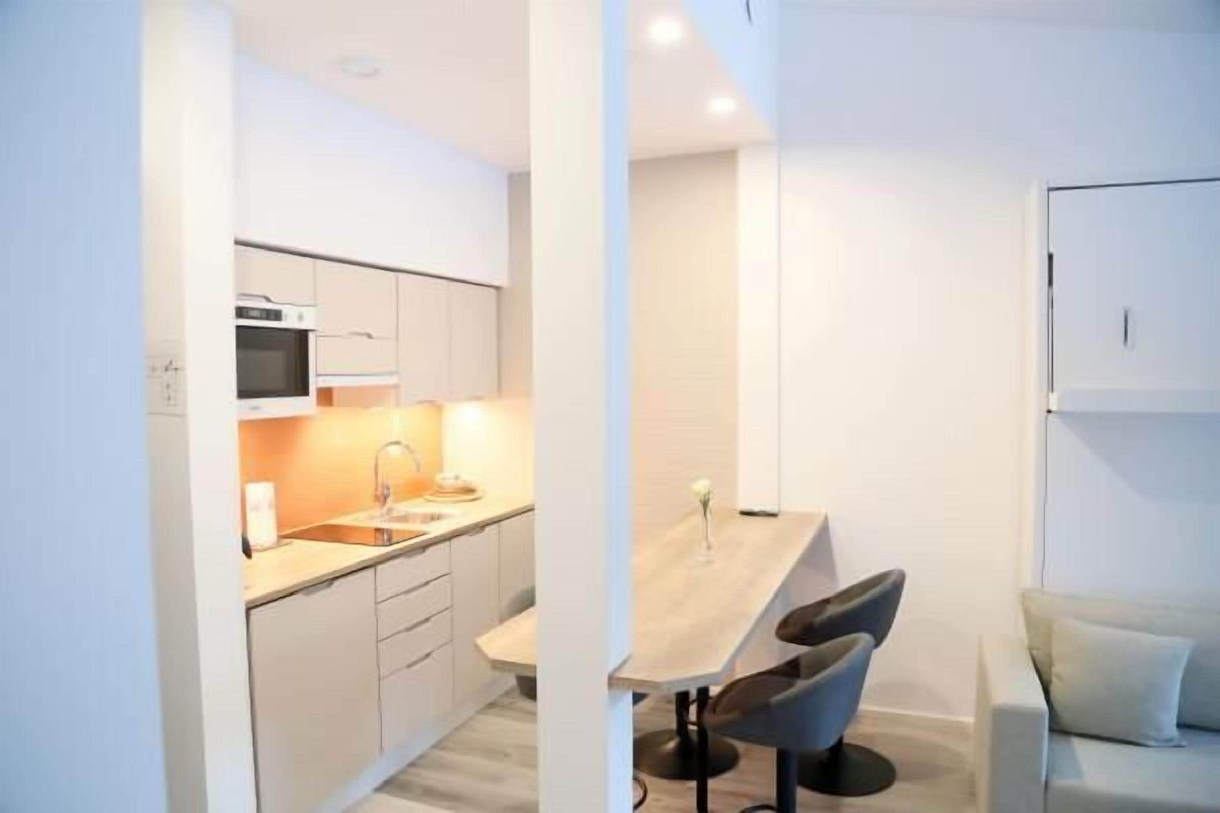 Una cocina moderna con armarios blancos, una mesa de comedor de madera y dos taburetes de bar.