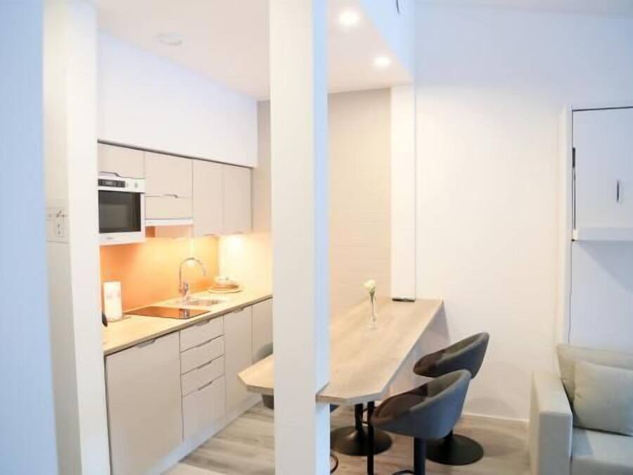A modern kitchen with white cabinets, a wooden dining table, and two bar stools.