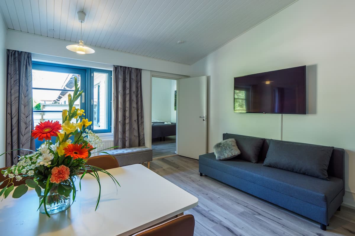 Ett modernt vardagsrum med en soffa, ett matbord med en vas med blommor och ett stort fönster med gardiner.