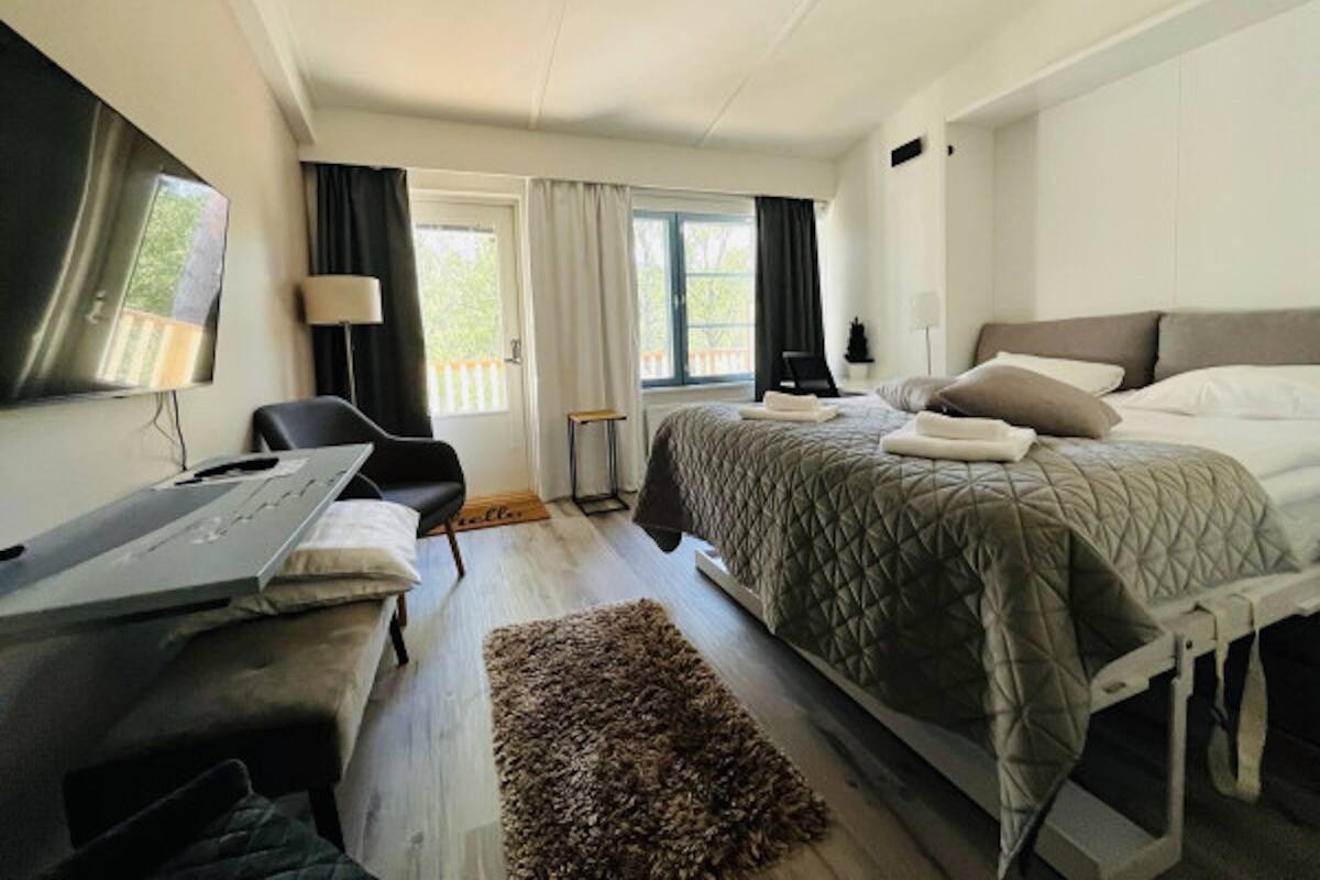 Ett hotellrum med en säng, ett skrivbord, en stol, en tv och ett fönster med gardiner.