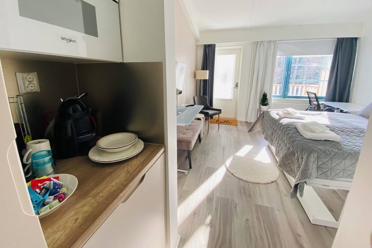 Ett hotellrum med ett litet kök, en säng med handdukar, ett skrivbord och utsikt över omgivningarna.