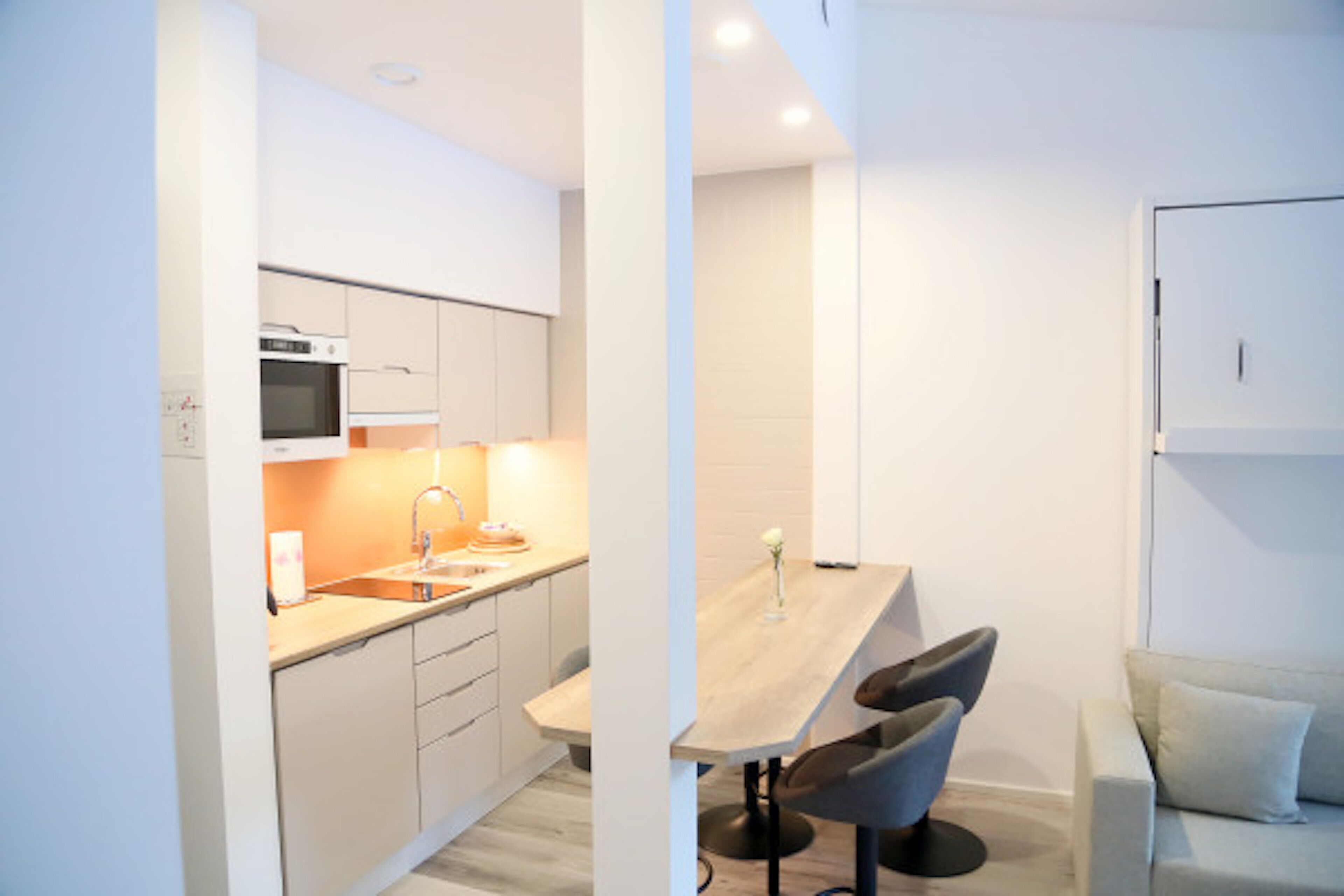 Una cocina moderna con armarios blancos, encimera de madera y comedor con mesa y dos sillas.
