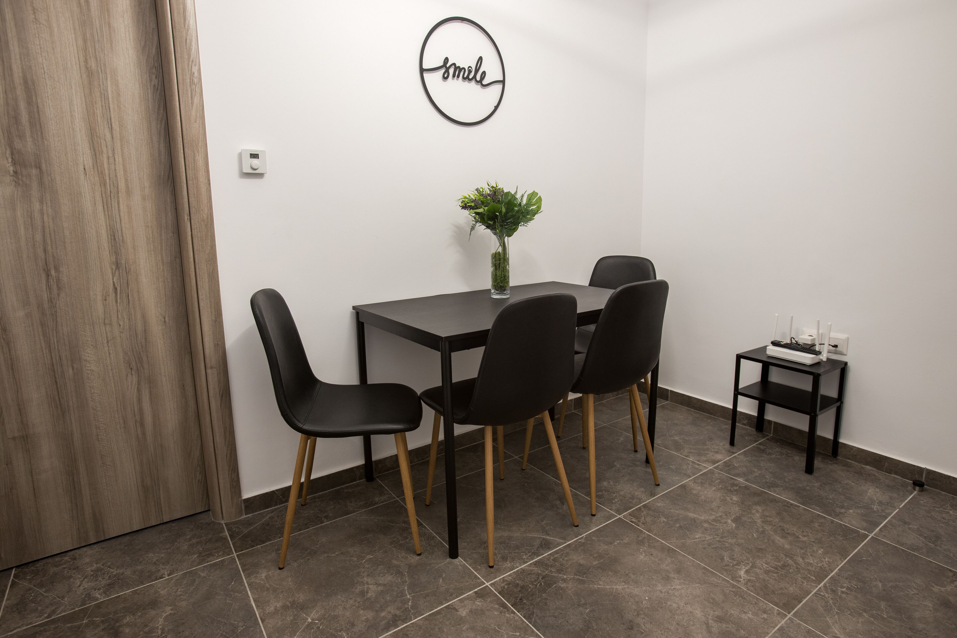 A dining area with a table, four chairs, a vase with flowers, and a small side table with a candle.