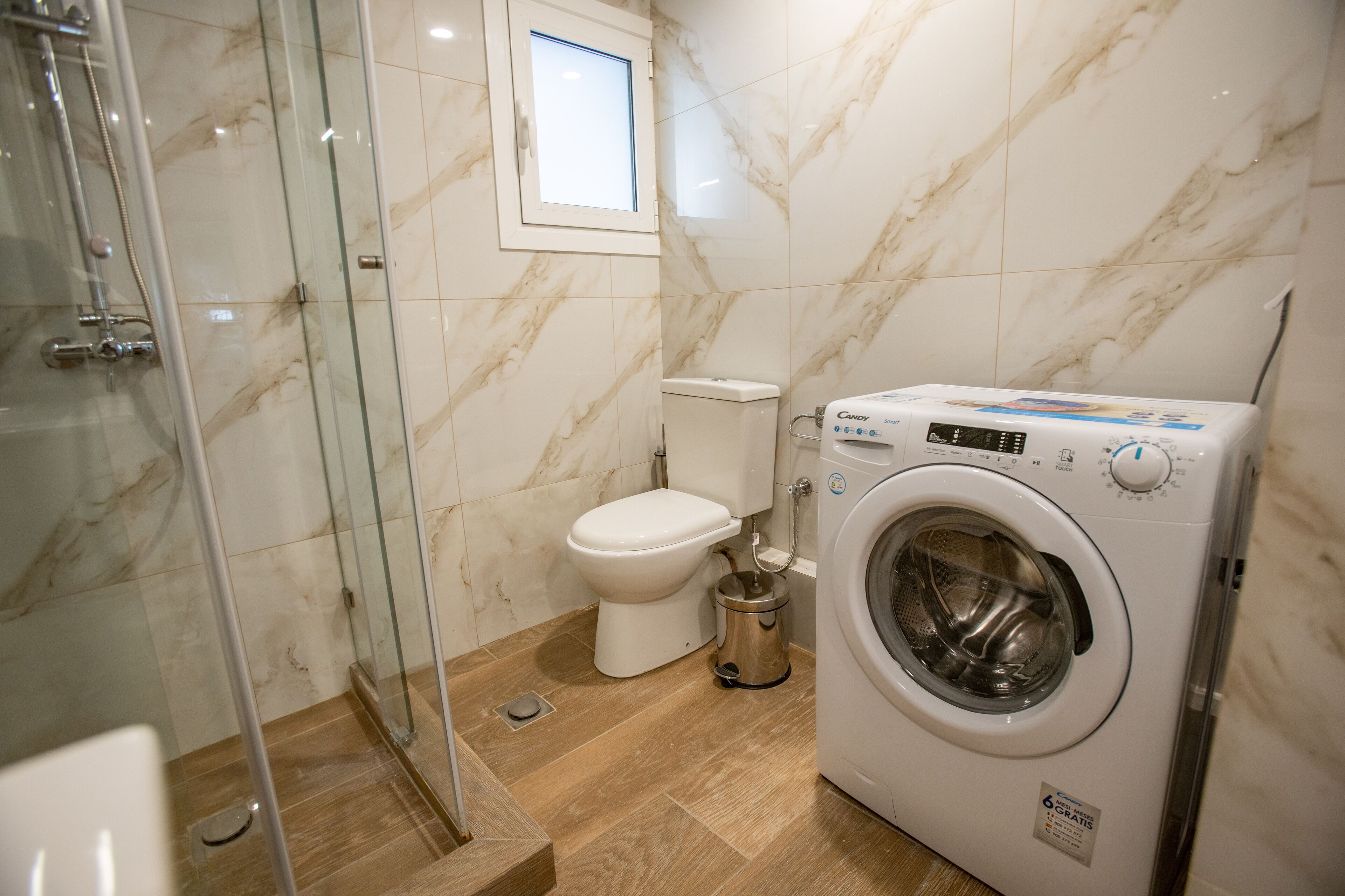 Un baño con cabina de ducha de vidrio, inodoro y lavadora de carga frontal.