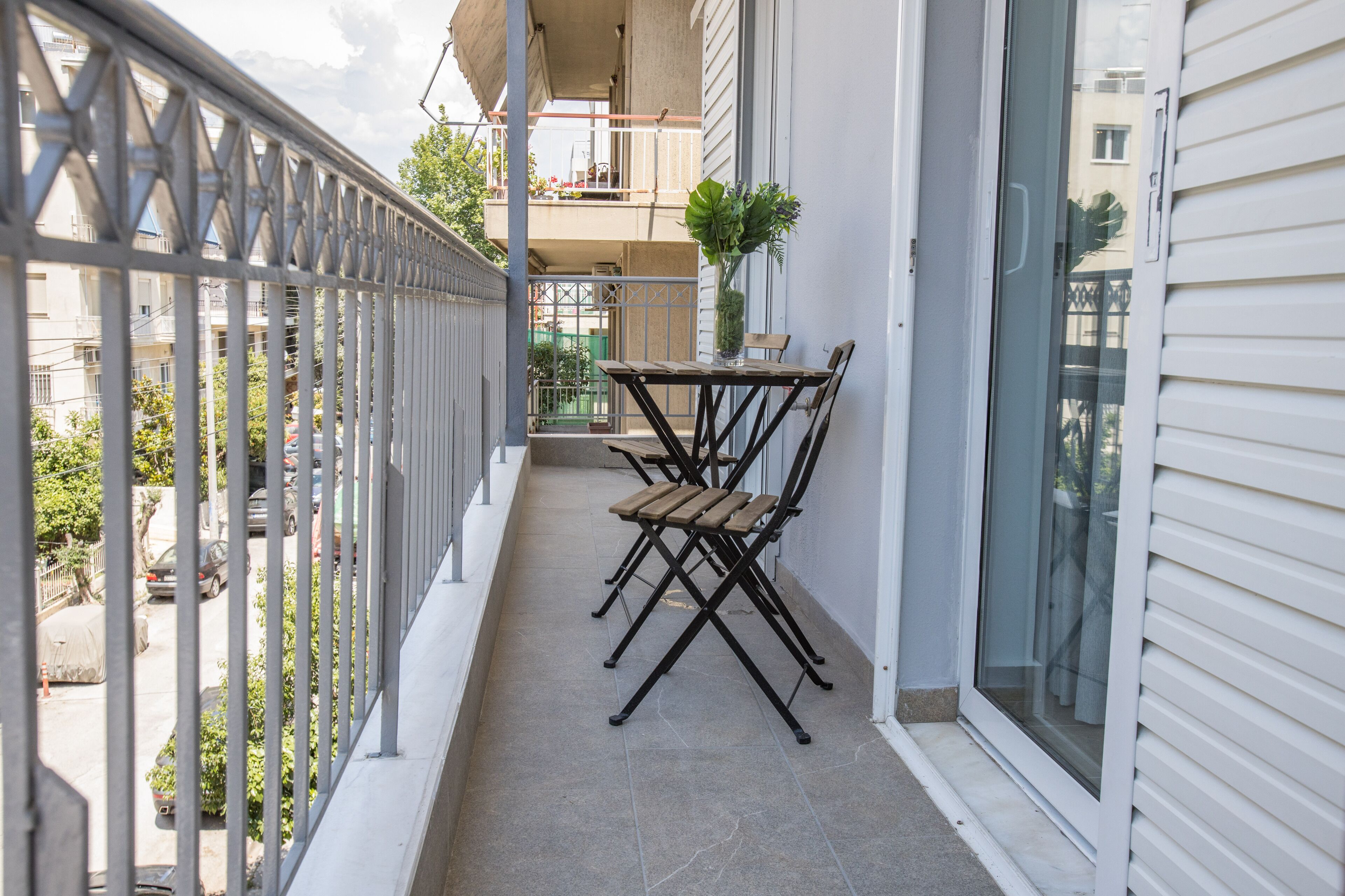 A balcony with a table and chairs, a potted plant, and a view of neighboring buildings.