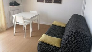En stue med et hvidt bord og stole, en grå sofa med mønstrede puder, et fladskærms-tv på et stativ, og et verdenskort som billedkunst på væggen.