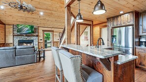A spacious living area with a fireplace, a bar with stools, and a kitchen with a stainless steel refrigerator. - Tyson’s Peak – Blue Ridge, GA. (Blue Ridge)