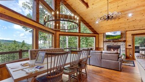 A spacious living area with a fireplace, large windows, and a wooden ceiling. - Tyson’s Peak – Blue Ridge, GA. (Blue Ridge)