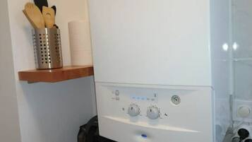 Una cocina con una estufa blanca, un estante de madera con utensilios de cocina y un recipiente metálico.