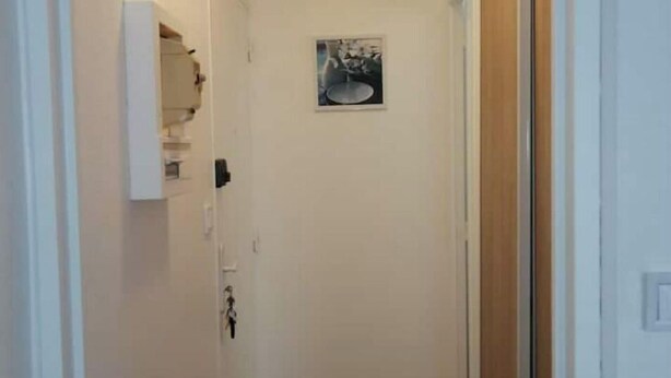 A narrow hallway with a wooden floor, white walls, and a small framed picture on the wall. - Studio Bienvenue Tout Confort (Orléans)
