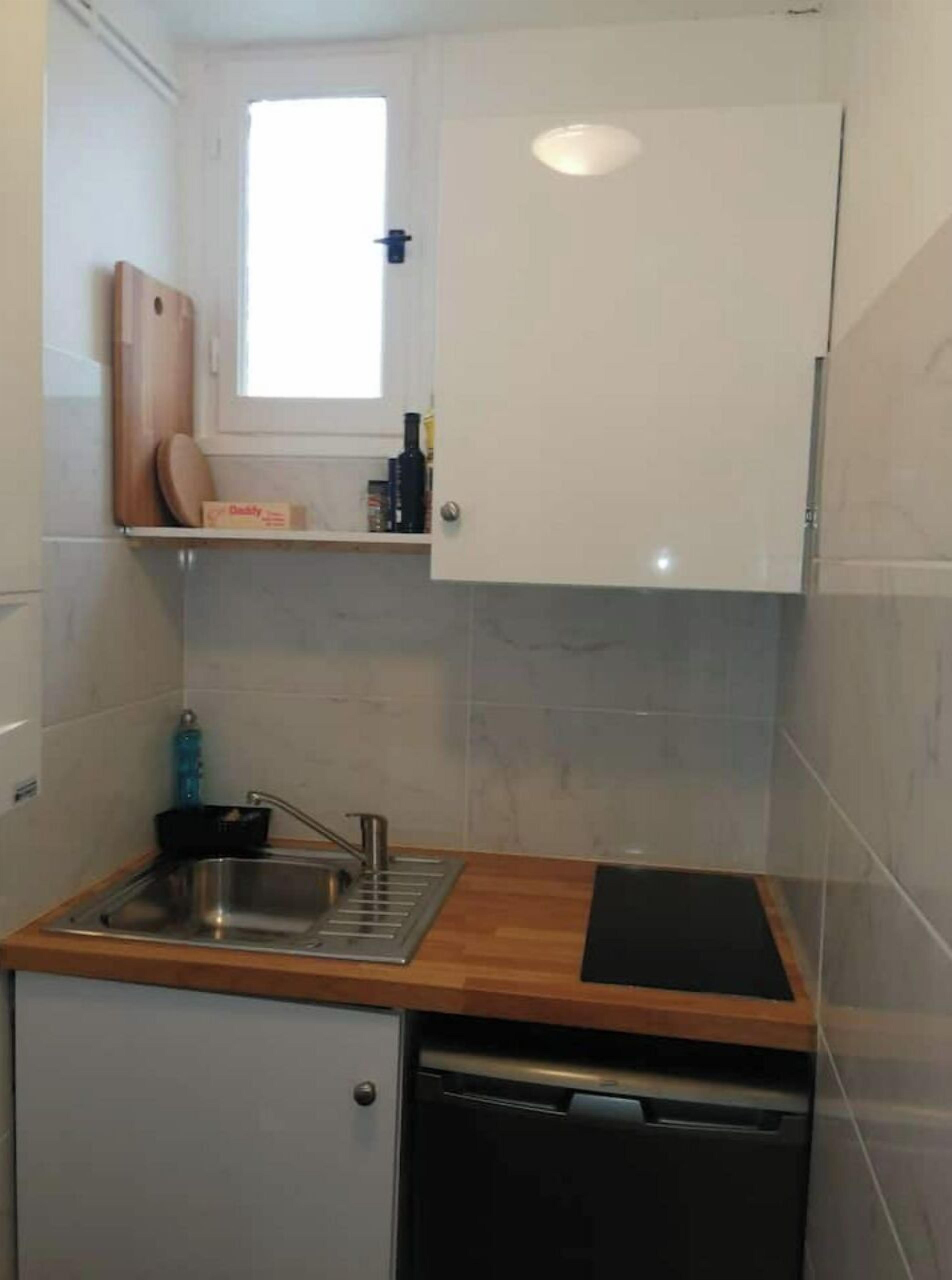 Eine kompakte Küche mit eingebautem Geschirrspüler, einem kleinen Fenster über der Spüle und einer Holz Arbeitsplatte.