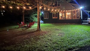 Una casa con un patio cubierto, luces colgantes y sillas rojas.