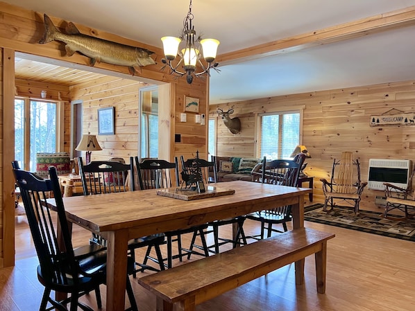 A wooden cabin interior with a dining table, chairs, a bench, a chandelier, and mounted animal heads.