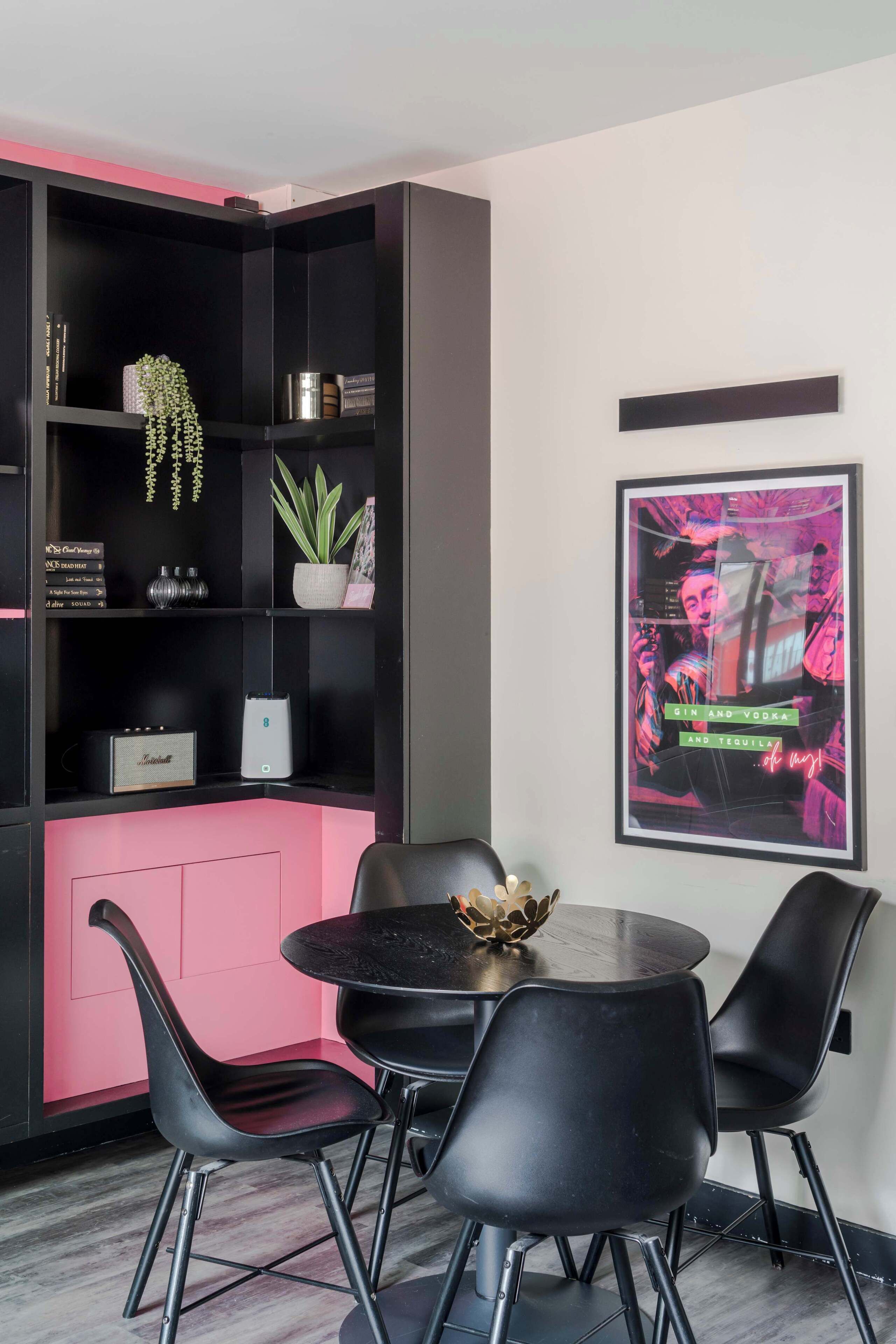 A modern room with a black bookshelf, a round table with chairs, and a framed poster on the wall.