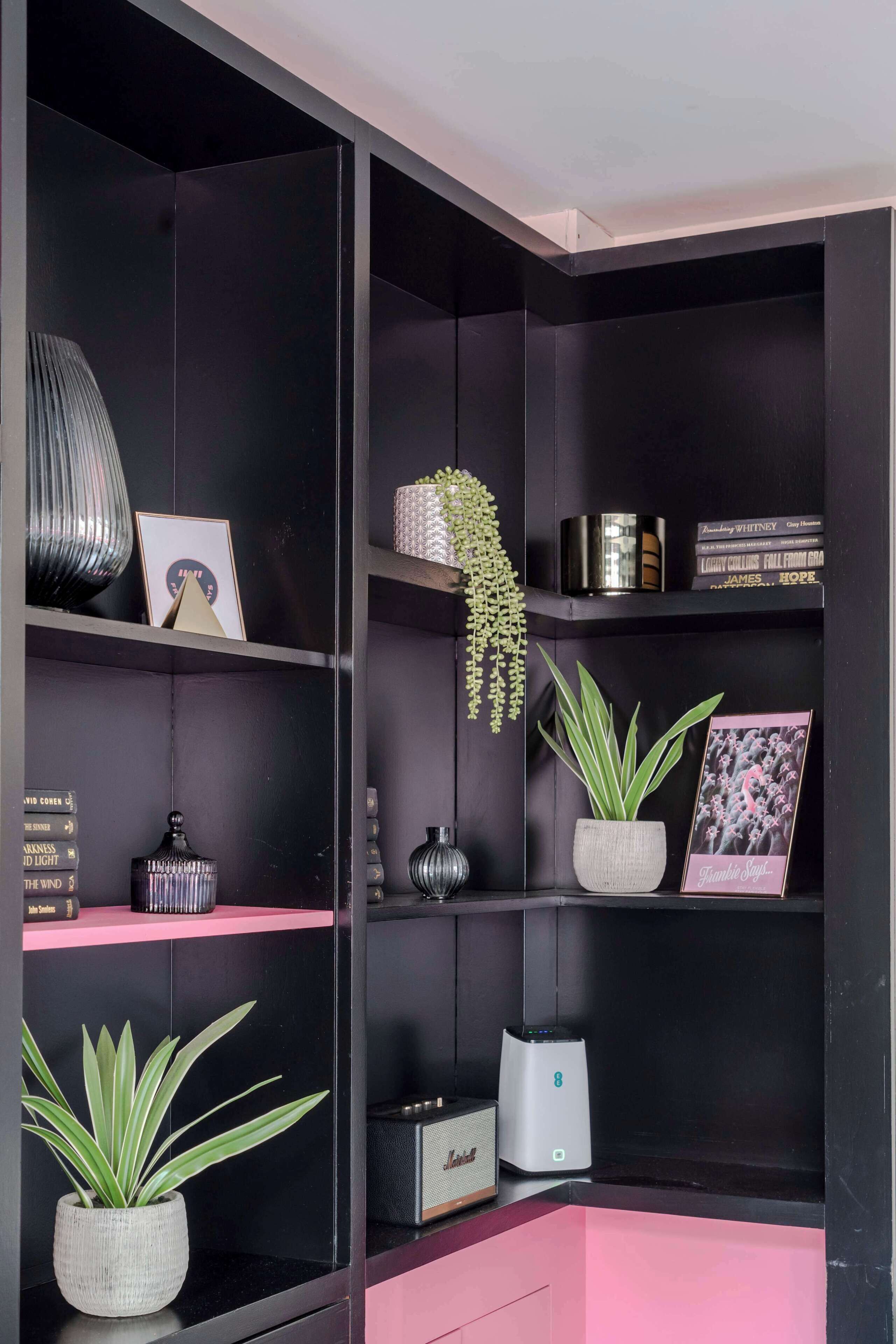 A black bookshelf with decorative items and a pink shelf.
