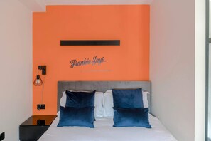 Un dormitorio con cama, dos almohadas, una mesita de noche, una lámpara de pared y una frase motivacional.