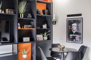 Een modern interieur met een zwarte boekenkast, een ronde tafel met stoelen, en een lijst met een afbeelding aan de muur.