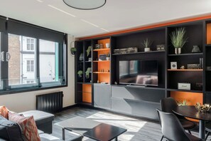Una sala de estar moderna con un ventanal grande, un televisor de pantalla plana y estanterías empotradas con plantas y libros.