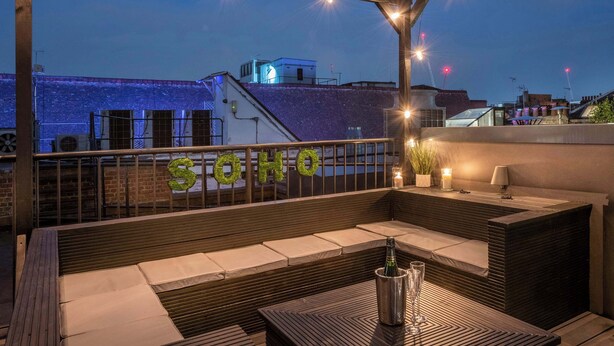 Un bar sul tetto con una pergola in legno, posti a sedere all'aperto, un'area bar e vista sulla città.