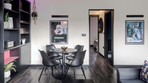 Un interno moderno con un'area pranzo che include un tavolo rotondo e sedie, una libreria con piante e due opere d'arte incorniciate alle pareti.