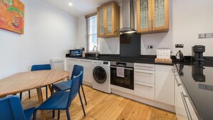 A compact kitchen with a washing machine, a stove, and a coffee maker. - Fitzrovia Duplex · 2-Bed · Private Patio Garden (London)